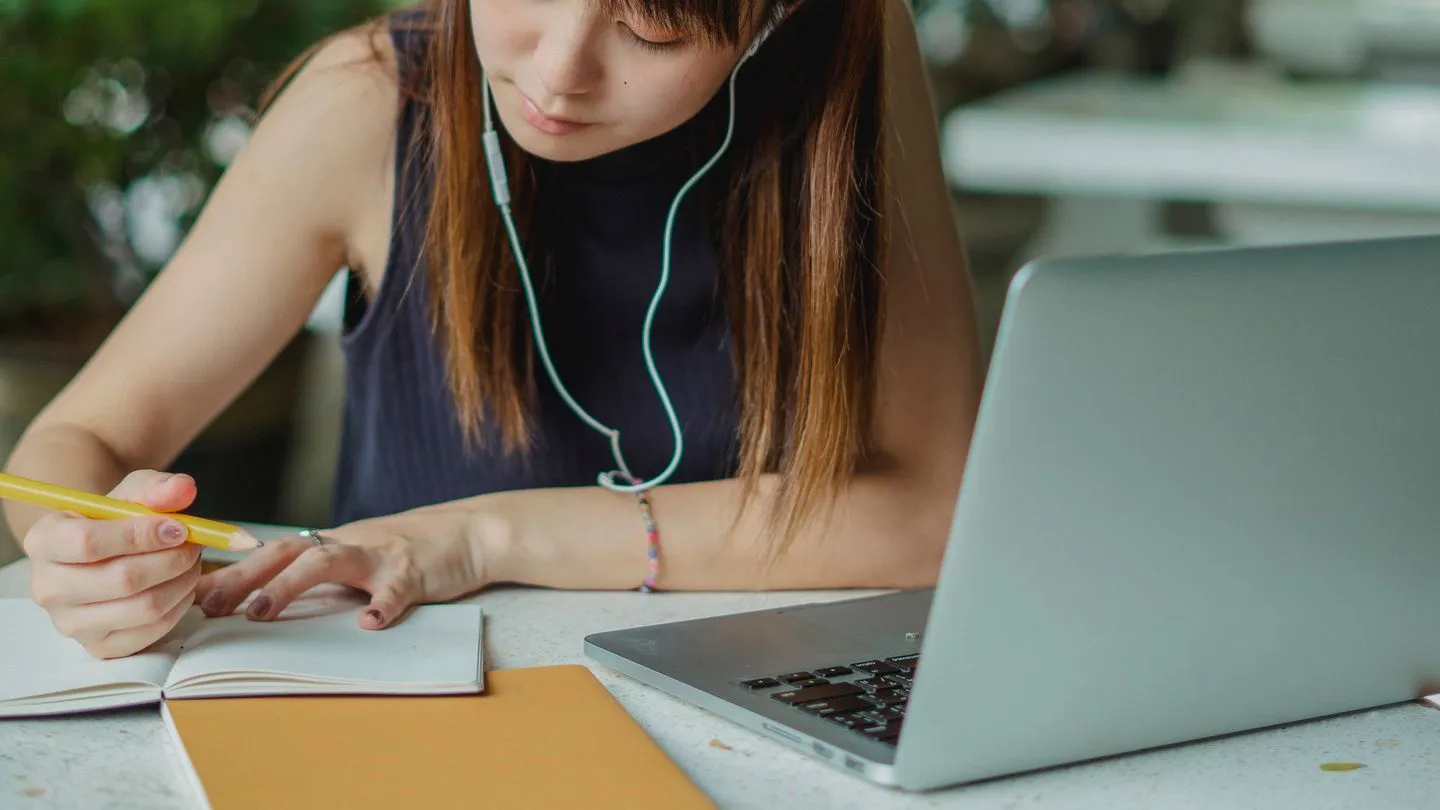 A student taking notes while learning on her laptop