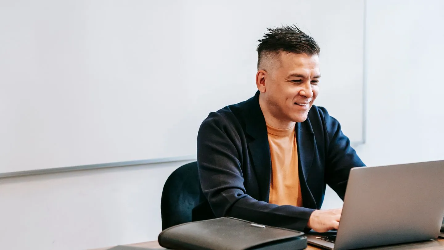A professional smiling calmly while reviewing work on his laptop